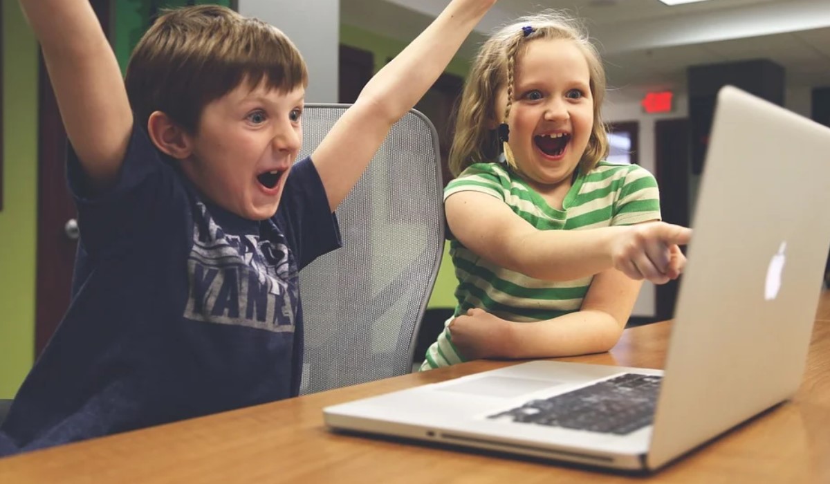 2 enfants contents avec bras levés devant un ordinateur