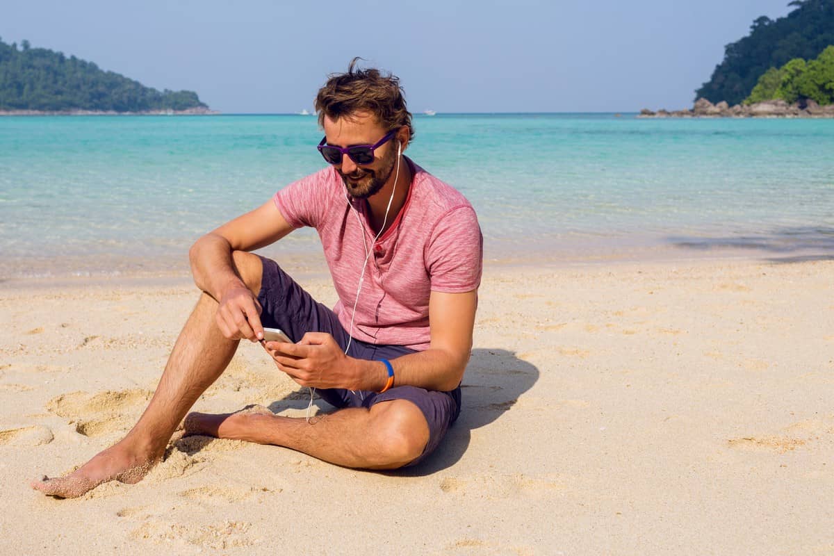 Un touriste sur une plage exotique écoute de la musique sur son téléphone