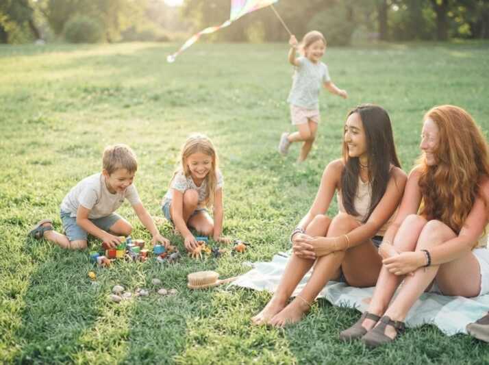 Deux femmes et trois enfants jouent dans un parc sur une pelouse.
