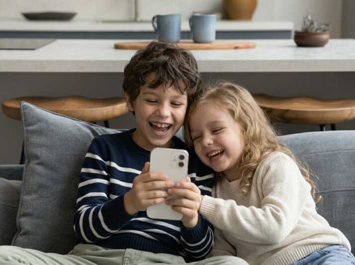Un garçon et une fille regardent un smartphone en riant sur un canapé.