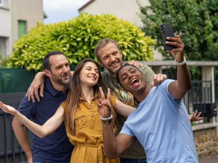 Quatre personnes prennent un selfie avec un smartphone Samsung Galaxy S23 en extérieur.