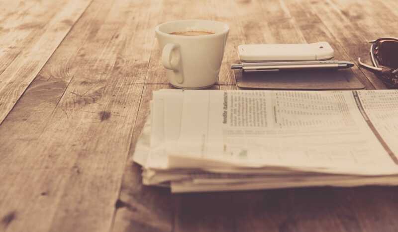un journal avec un smartphone et un café posé sur une table