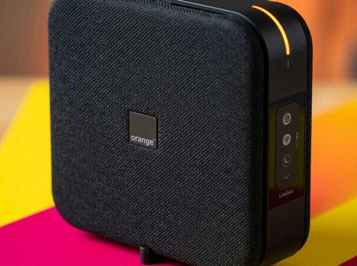 Vue rapprochée d'une box internet Orange Livebox noire avec voyant lumineux orange sur le côté.