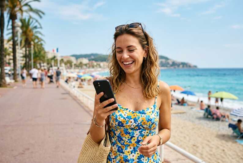 Personne souriante tenant un smartphone en extérieur pendant l'été.