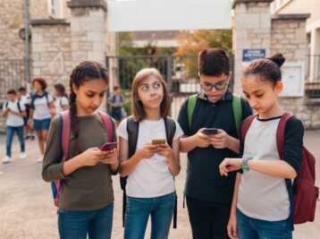 Quatre collégiens de 11 à 14 ans devant une école, utilisant des smartphones et une montre connectée.