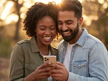 Un homme et une femme regardent ensemble un smartphone en souriant à l'extérieur.