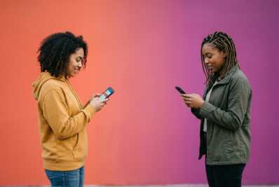 Deux personnes se faisant face, chacune tenant un smartphone, sur un fond dégradé orange et violet.