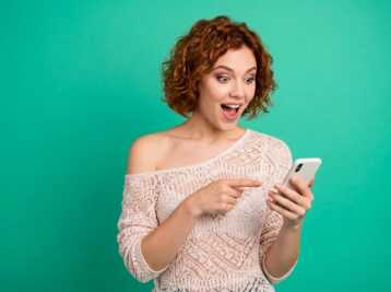 Femme aux cheveux roux regardant son téléphone sur fond vert.