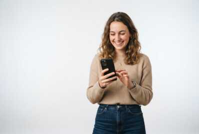 Jeune femme souriante utilisant un smartphone noir sur fond blanc.