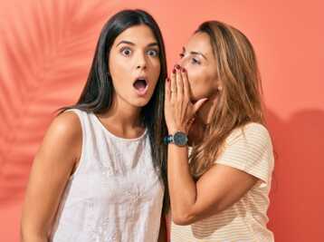 Deux femmes sur fond orange, l'une chuchote à l'oreille de l'autre qui a une expression surprise.