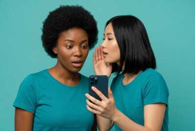 Deux femmes regardant un smartphone sur fond uni.