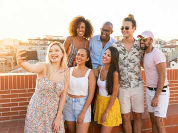 Groupe de sept personnes en tenue d'été prenant un selfie sur un toit en terrasse.