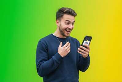 Homme de 20 ans tenant un smartphone avec une expression de surprise sur fond dégradé vert et jaune.