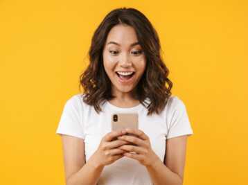 Jeune femme regardant son smartphone avec la bouche ouverte sur fond jaune.