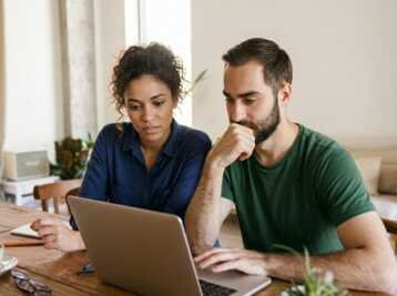 Un homme et une femme travaillent ensemble sur un ordinateur portable à une table en bois.