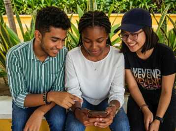 Trois jeunes adultes regardent ensemble un smartphone en extérieur.