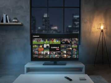 Téléviseur affichant l'interface mosaïque de Canal+ dans un salon avec une lampe sur pied.