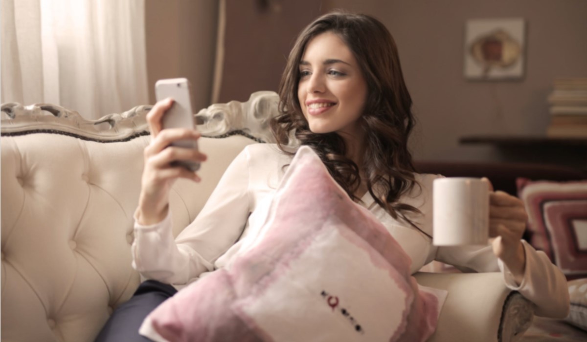 jeune femme assise dans son canape avec son smartphone et une tasse a la main