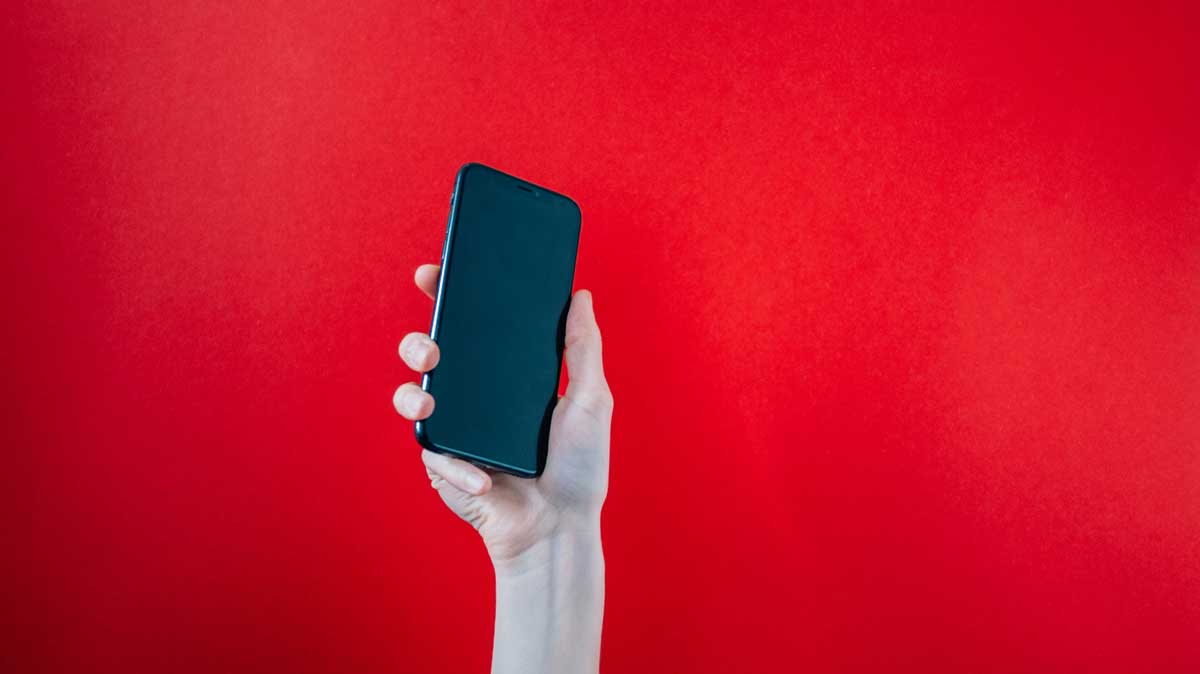 main tenant un smartphone sur fond rouge