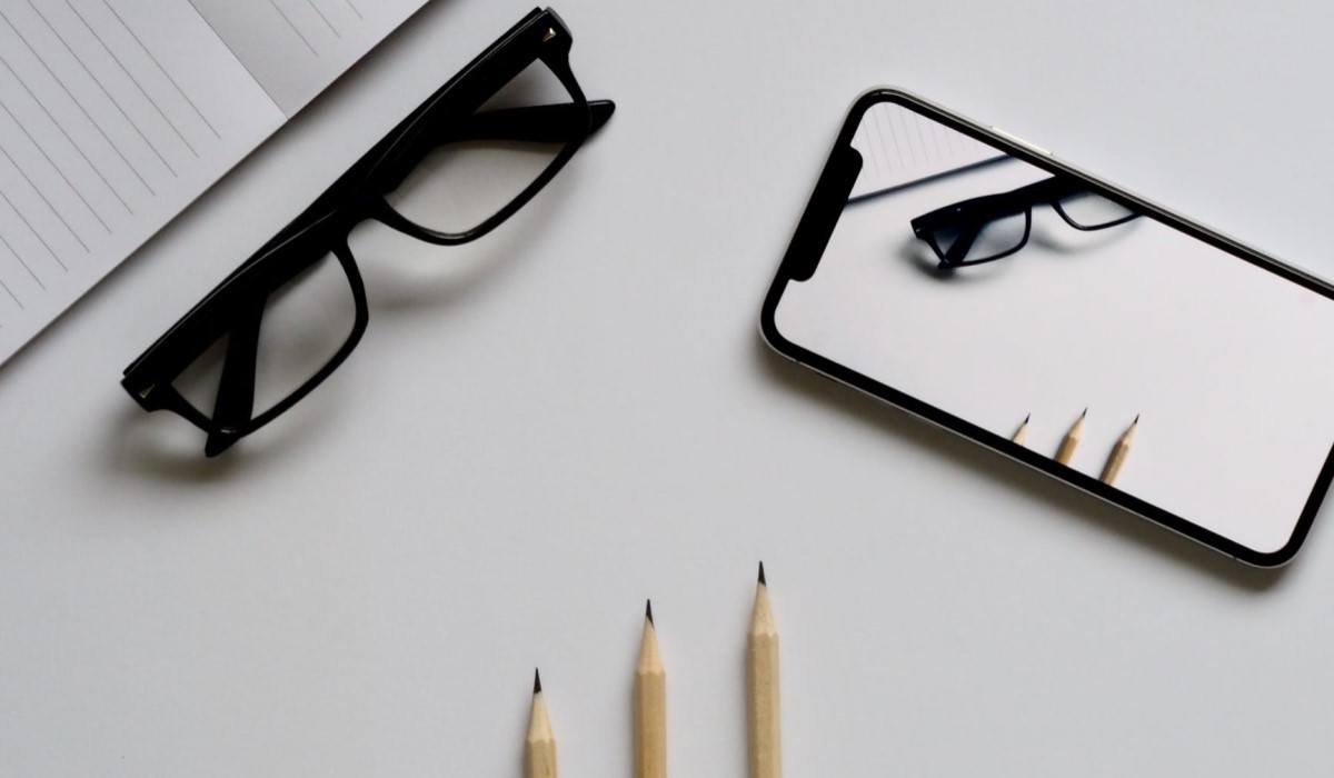 un smartphone, bloc note et une paire de lunette posé sur une table