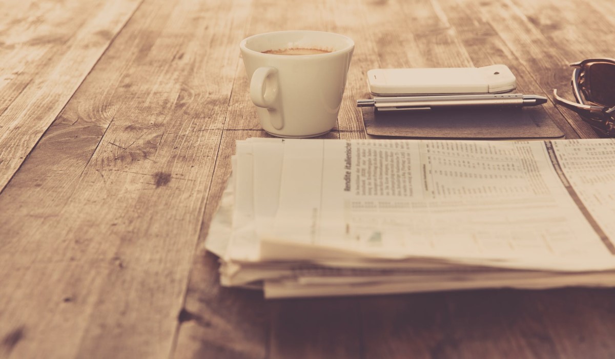un journal avec un smartphone et un café posé sur une table